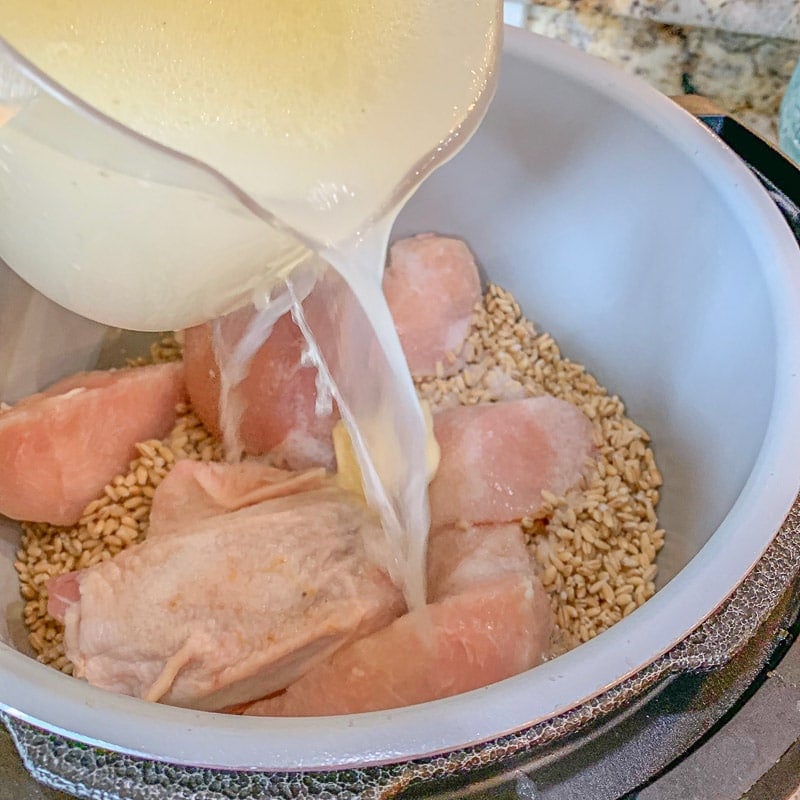 pouring broth over chicken and barley in instant pot