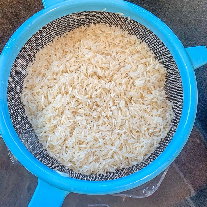 rice being strained in a blue strainer