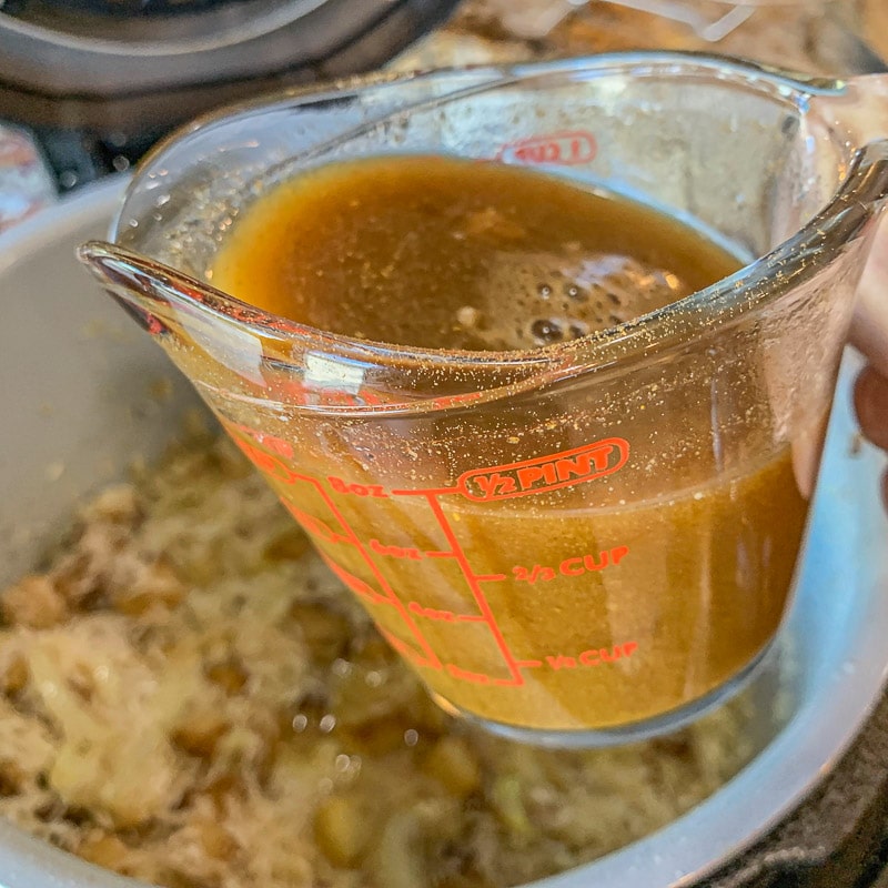 pouring broth from measuring cup into instant pot with biryani ingredients 