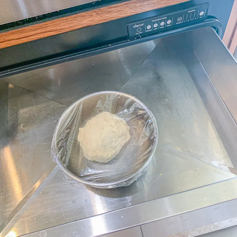 dough in a silver bowl covered in Saran Wrap