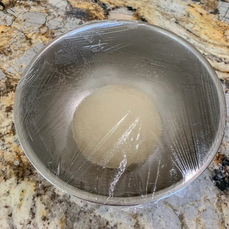 smooth dough in a bowl covered with Saran Wrap