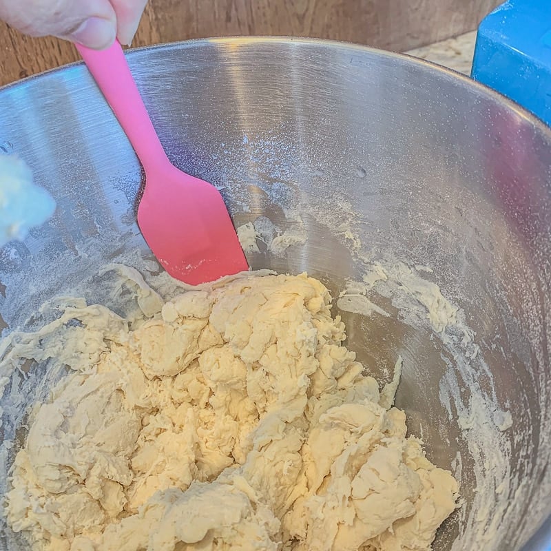 scraping sides of bowl of dough with a pink spatula