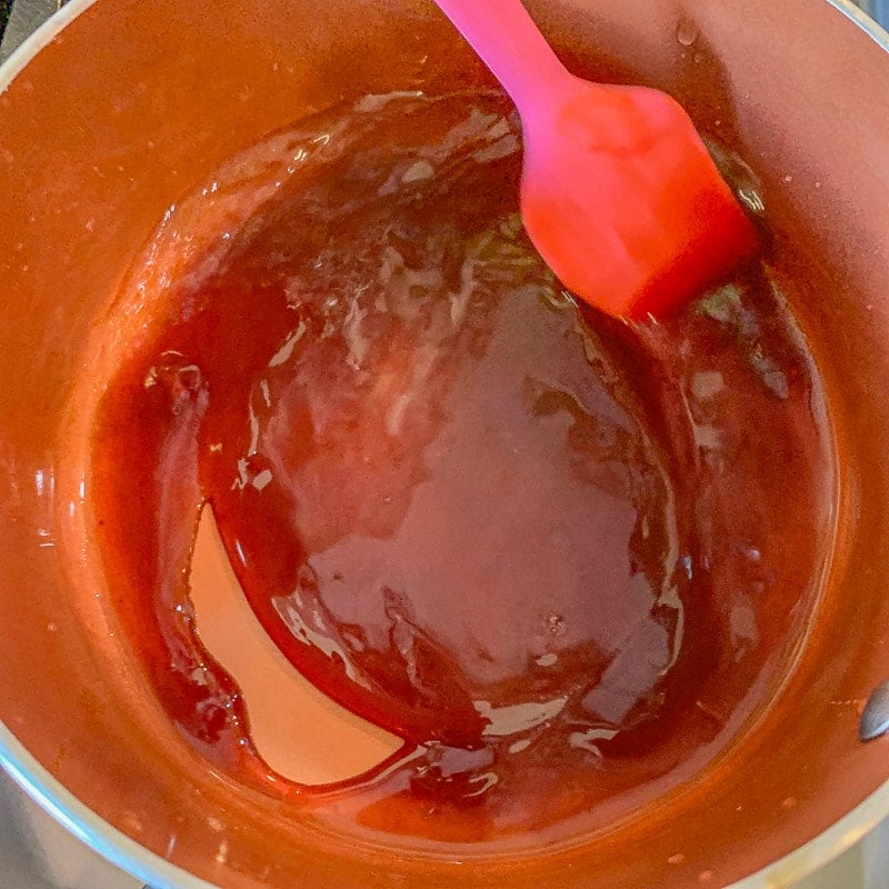 scraping date syrup off the bottom of a pot with a pink spatula 