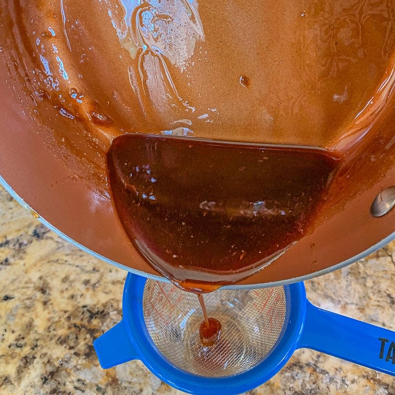 pouring syrup through a blue strainer 