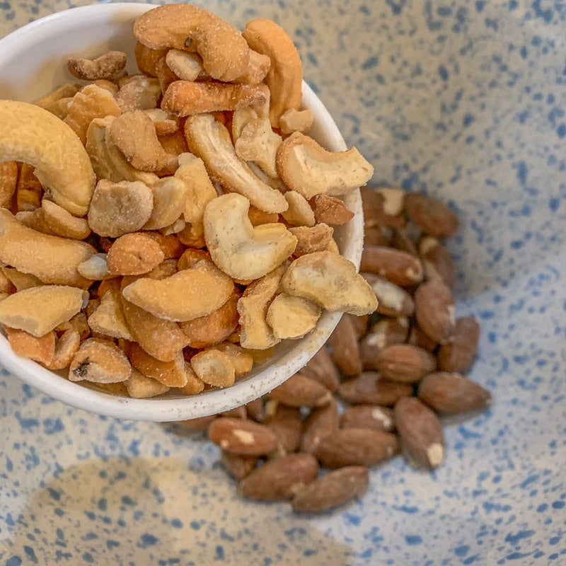 adding cashews to a bowl of almonds