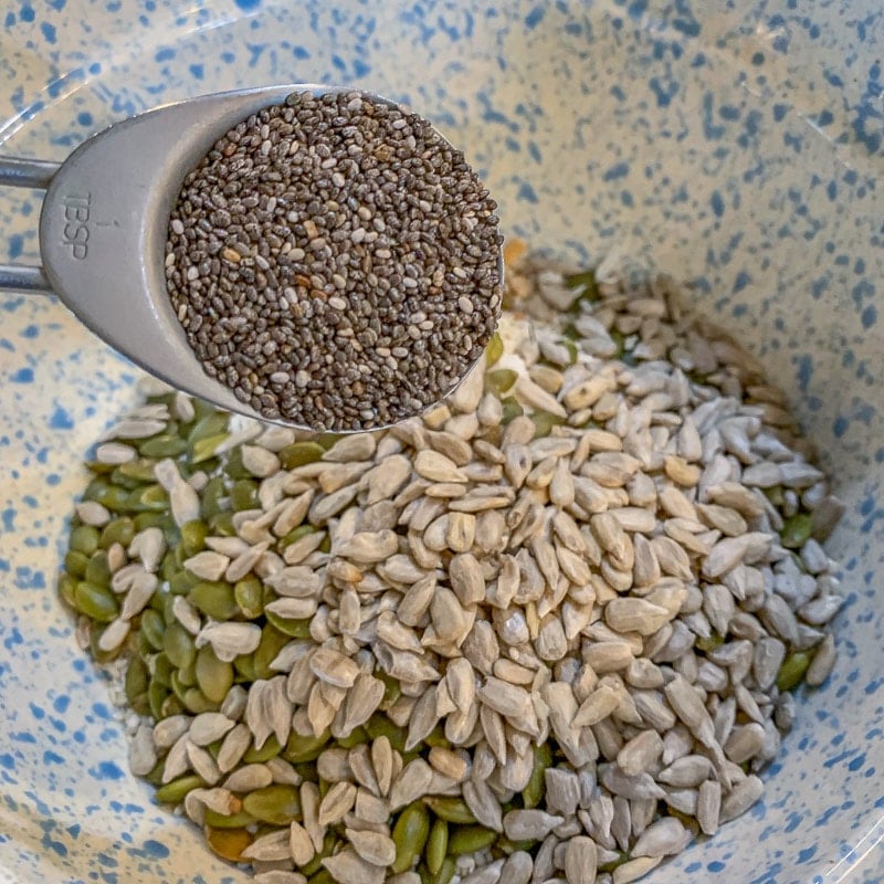 adding chia seeds to a bowl full of sunflower seeds and pumpkin seeds