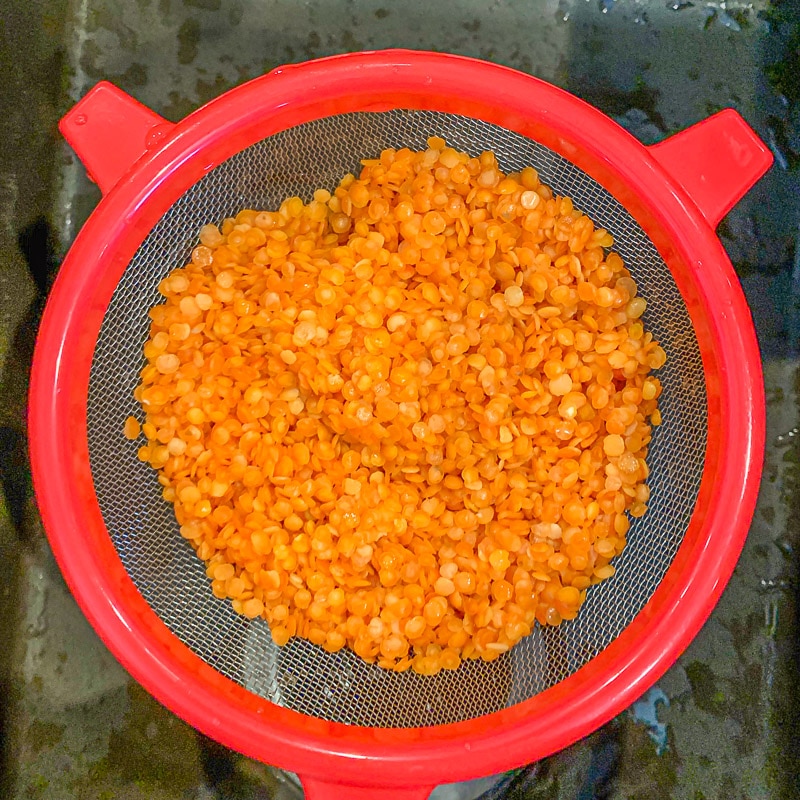 red strainer with orange lentil inside
