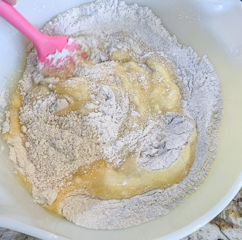folding wet ingredients into dry ingredients for classic banana bread with a pink spatula
