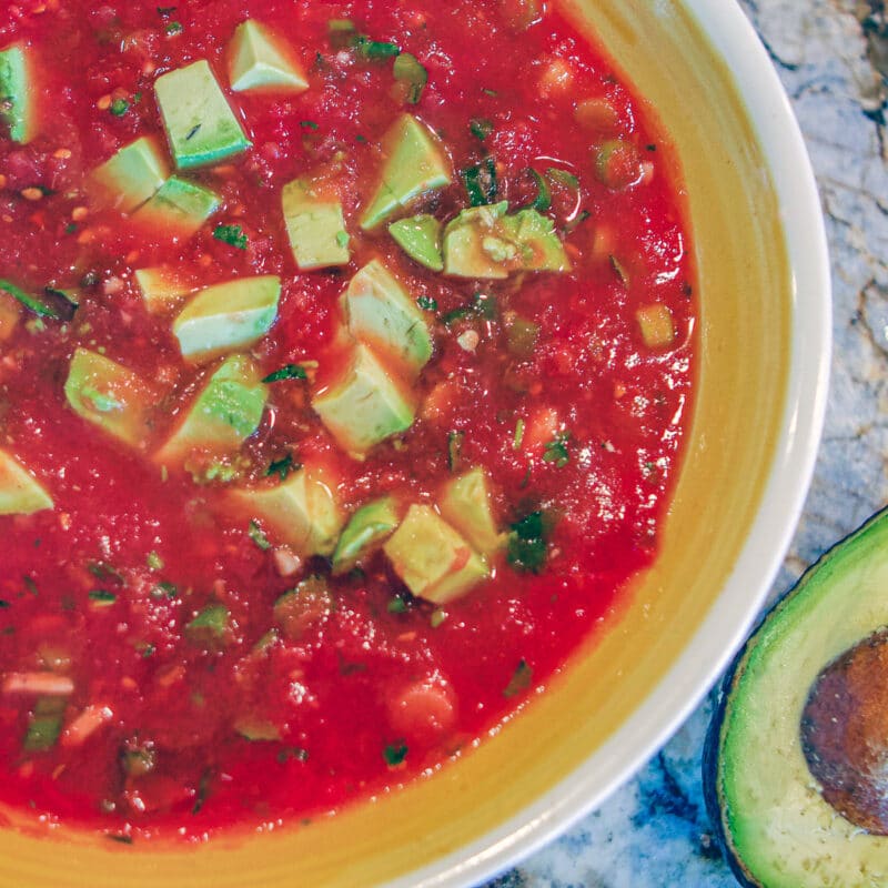 mexican salsa in a bowl with a yellow rim and a sliced avocado on the side