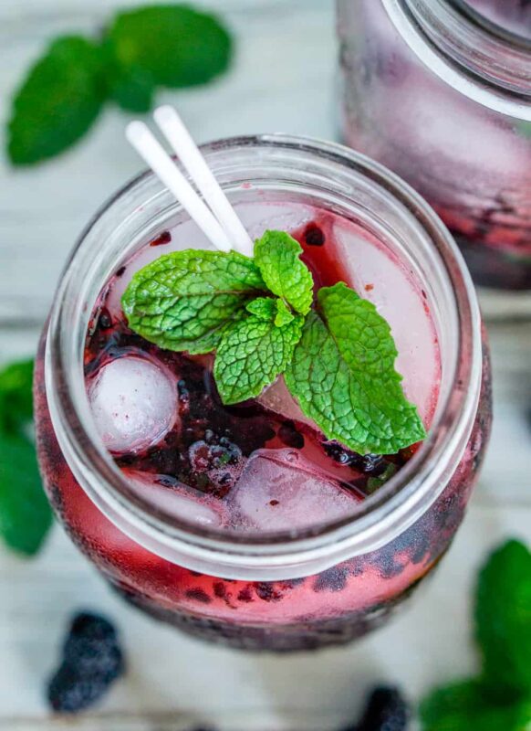 mulberry mojito in a glass with mint garnish and two white straws