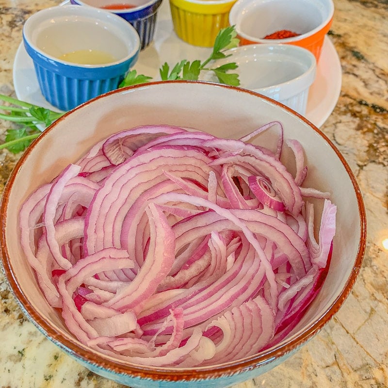 sliced onions in a bowl with small bowls behind it
