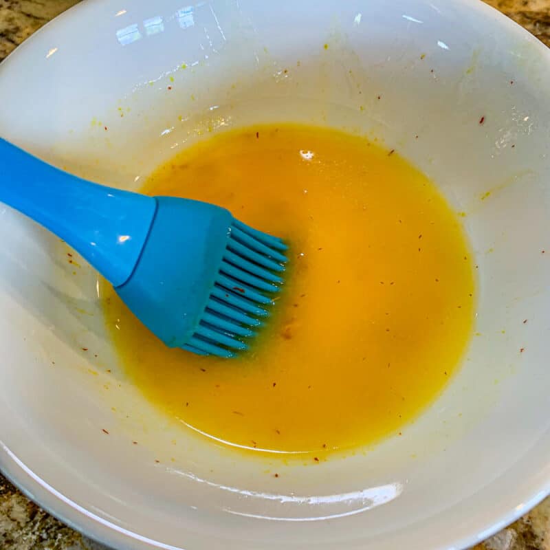 saffron butter in a white bowl with a blue basting brush