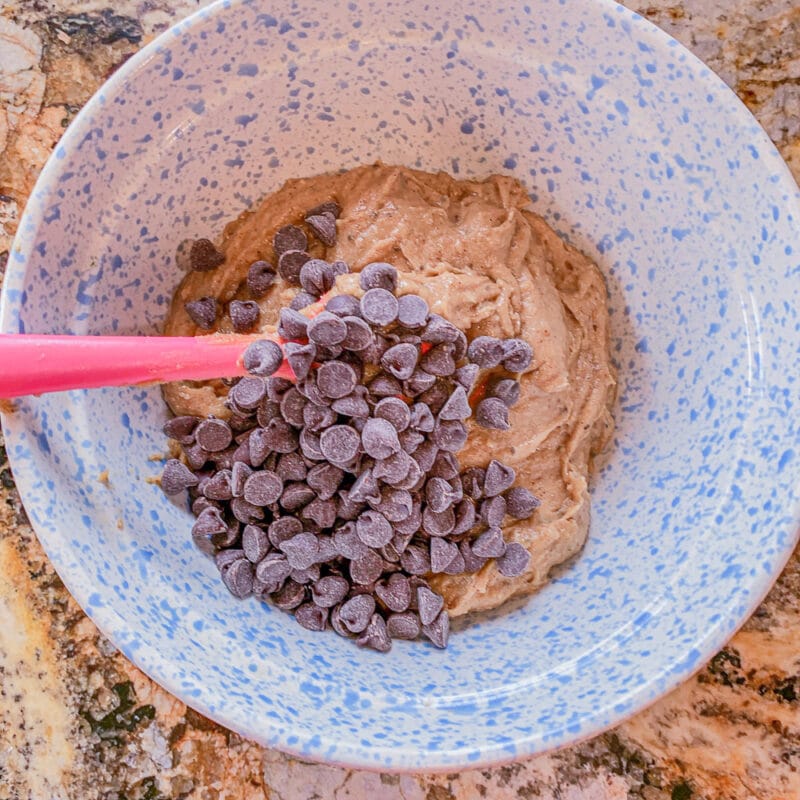 chocolate chips on top of chickpea dough in a blue dotted bowl 
