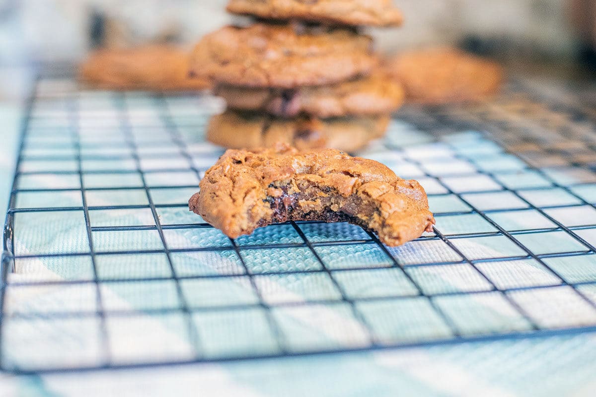 chickpea cookies on a cooling rack, one with a bite taken out over a blue and white towel