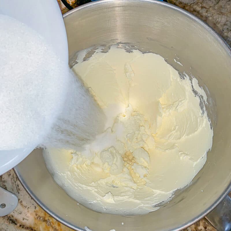 adding sugar to mixing bowl with cream cheese in it