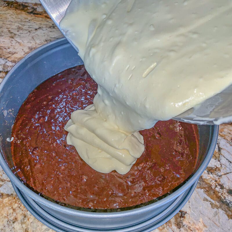 pouring cheesecake batter over brownie mix