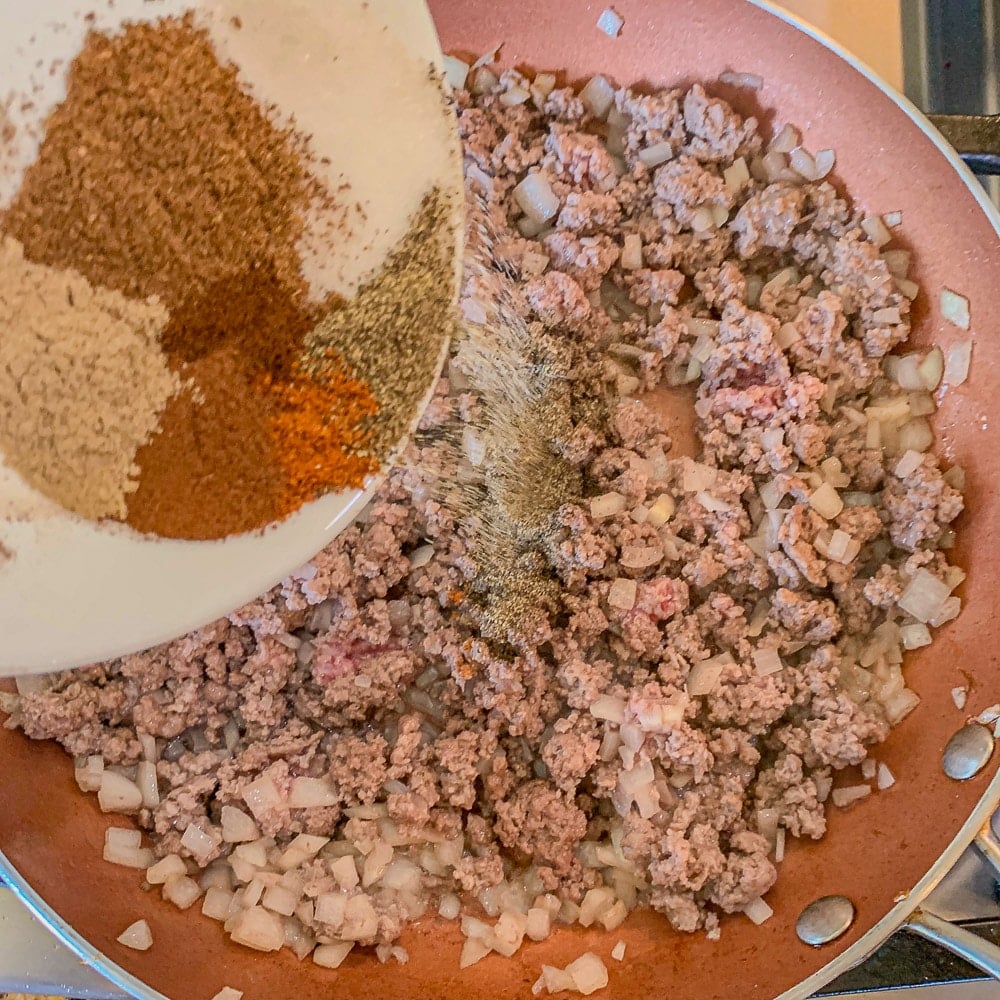 adding spices to ground beef and onions in a skillet