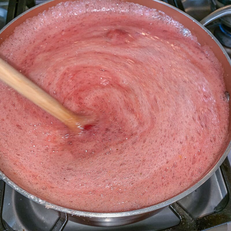 stirring foaming strawberry jam in a pot