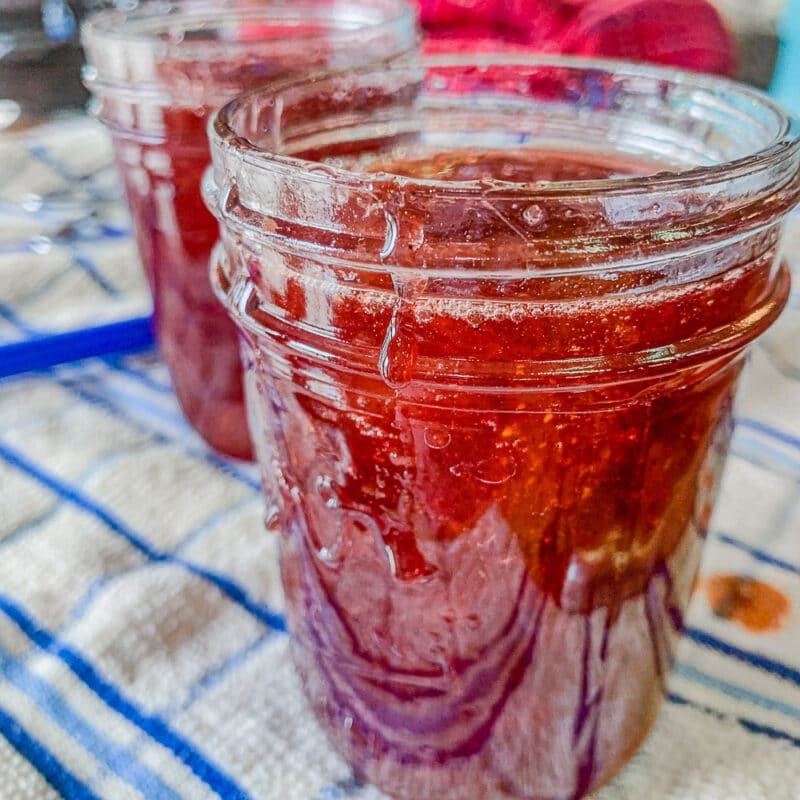 two jars of rhubarb strawberry jam on a blue and white striped towel