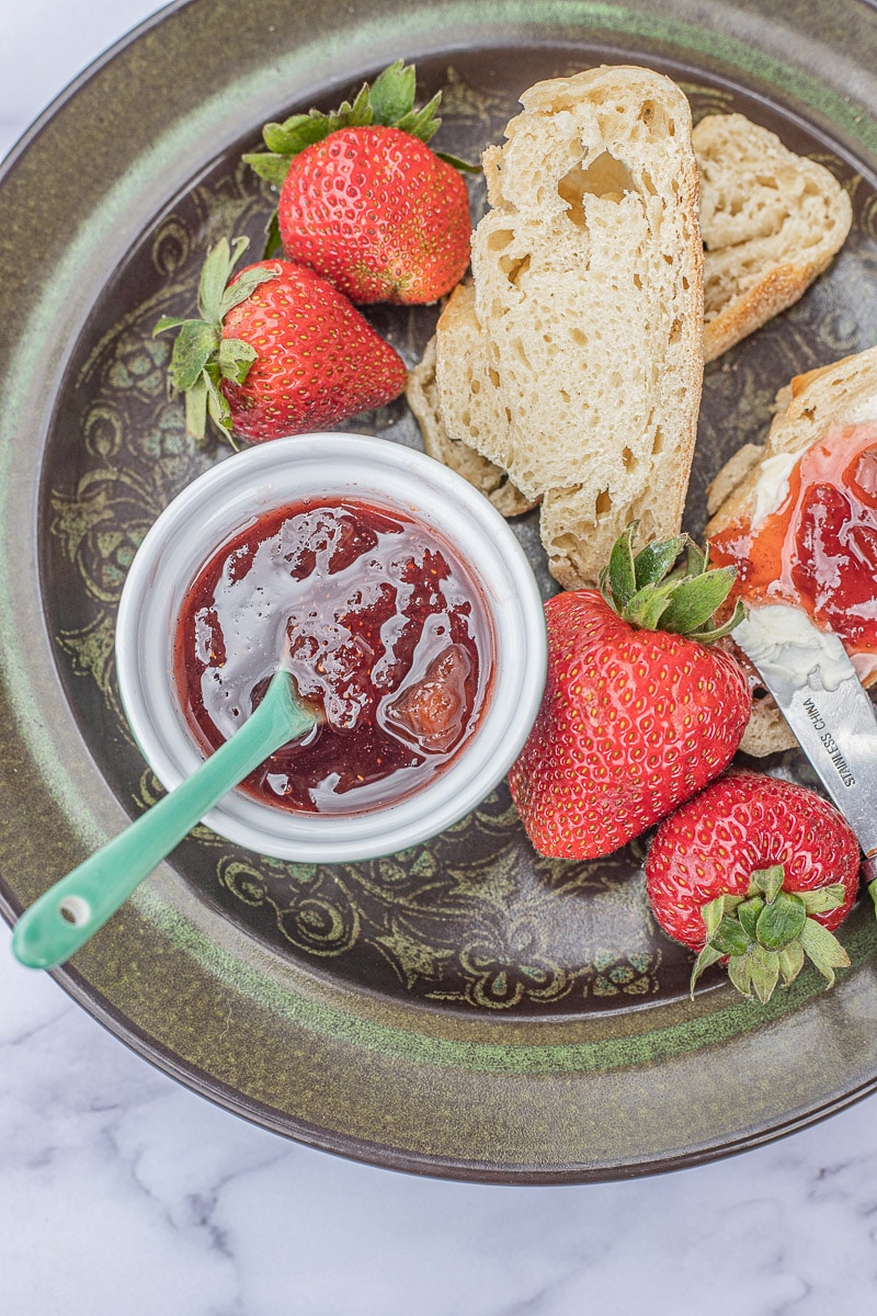 strawberry rhubarb jam in a small bowl with toast and fresh strawberries on a green plate