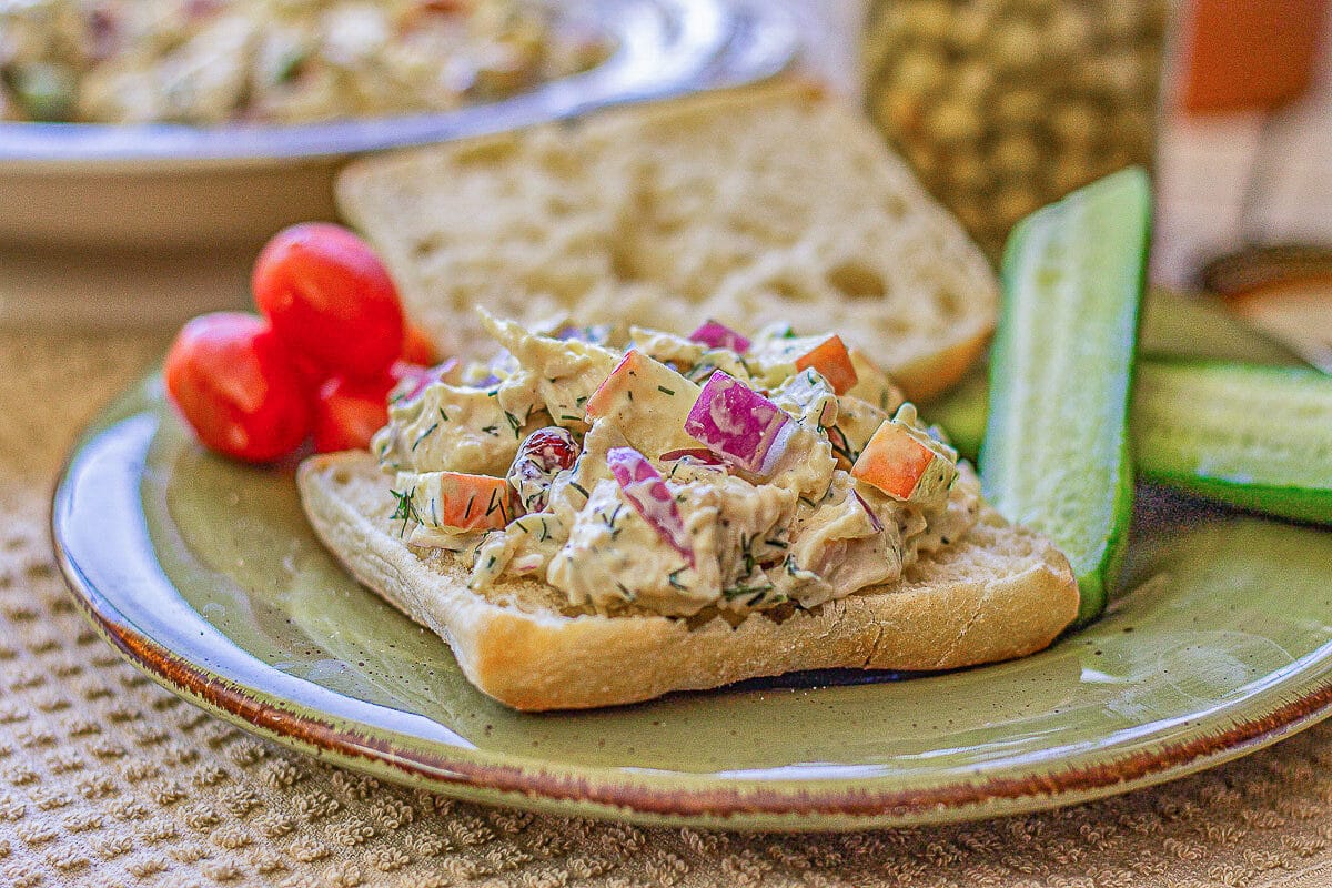 chicken salad sandwich with cucumbers and tomatoes on the side.