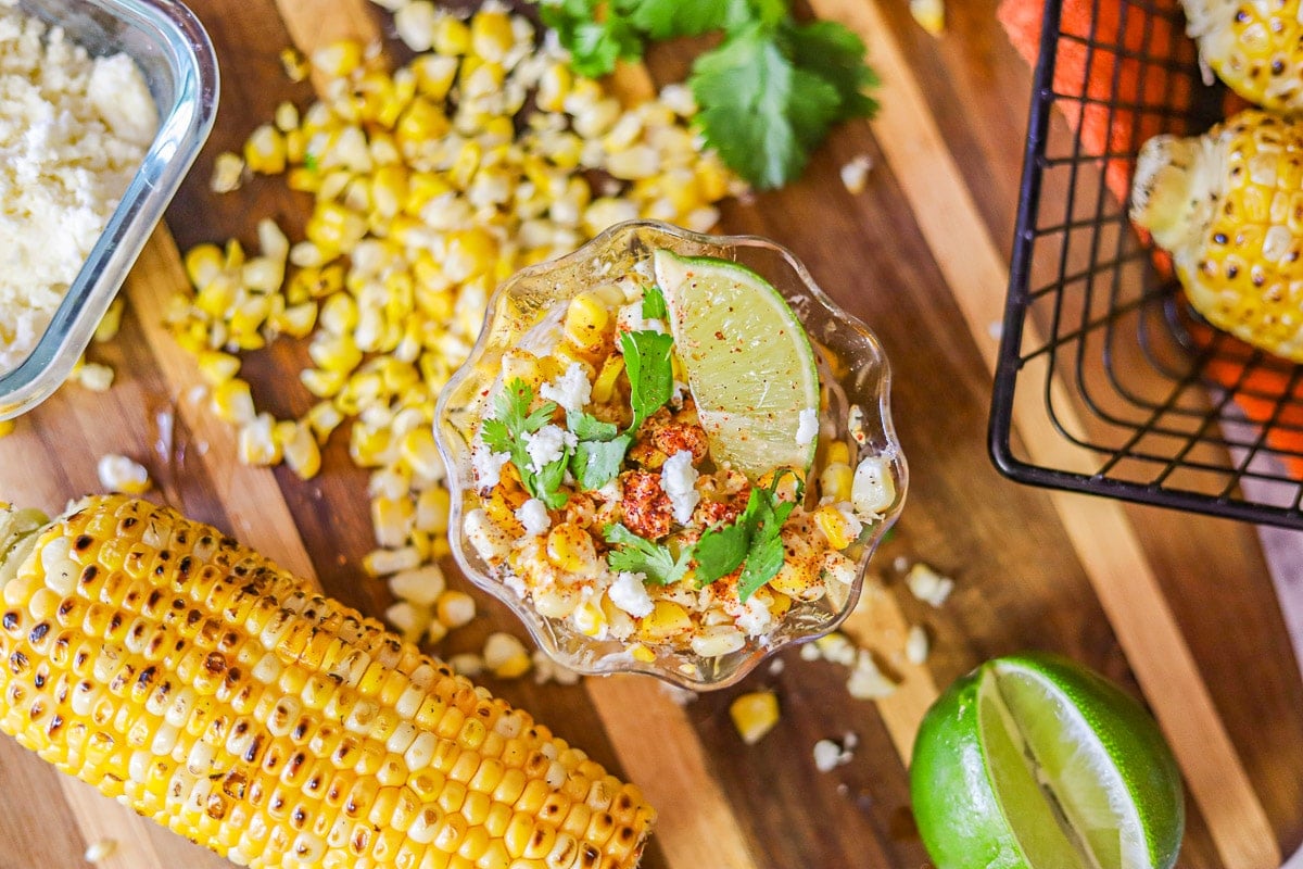 Mexican elote or corn in a cup with limes, cheese, and cilantro