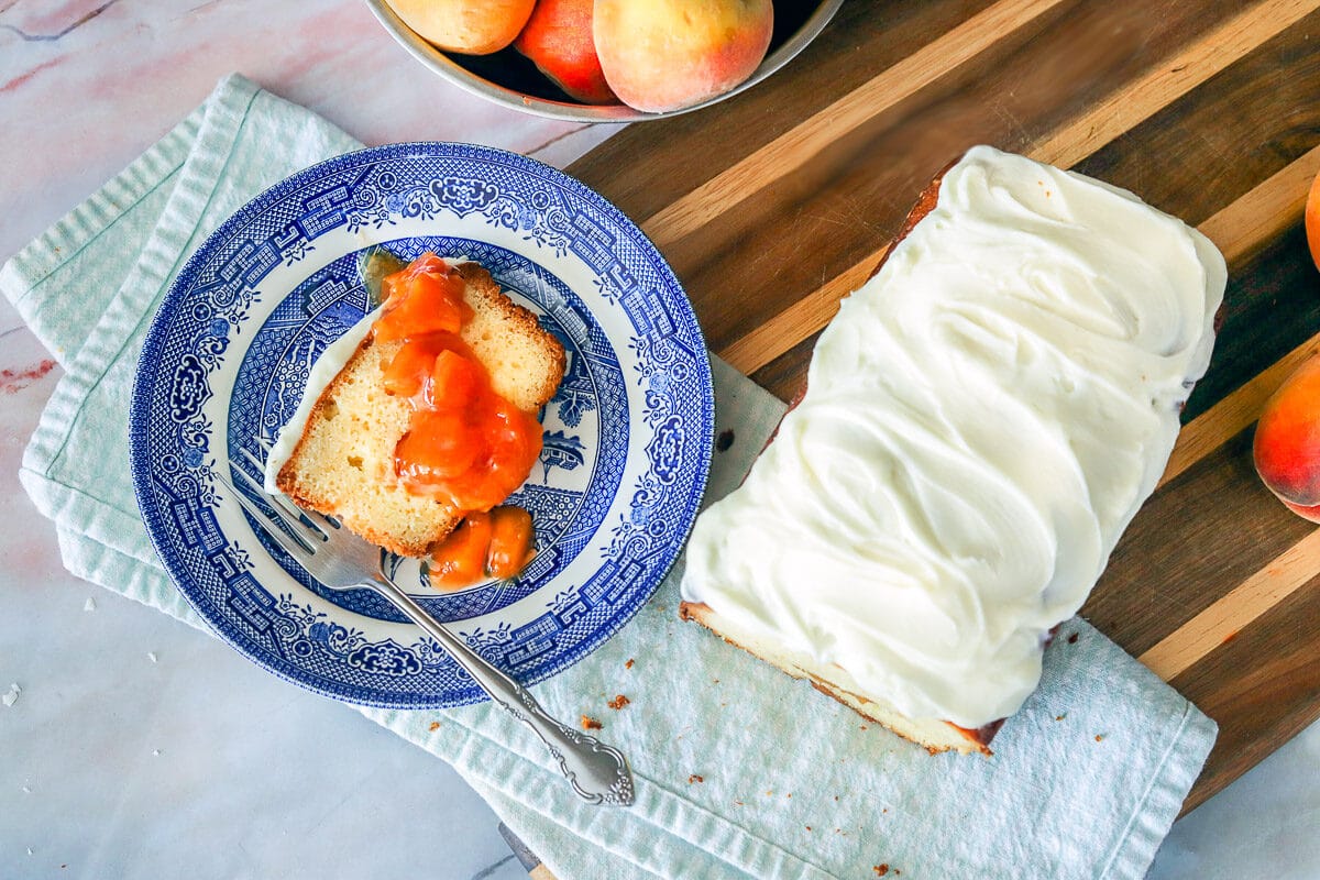 frosted Peach Cobbler Pound Cake with a slice on a blue plate with peaches around them