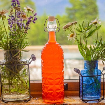 rhubarb gin in a bottle on a window with wild flowers on each side