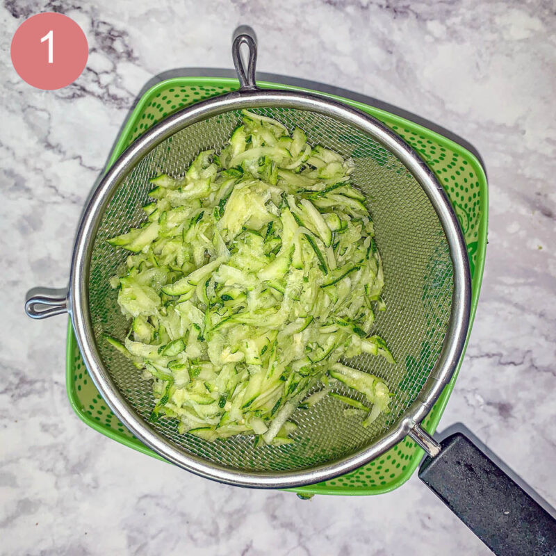 shredded zucchini being strained over a green bowl