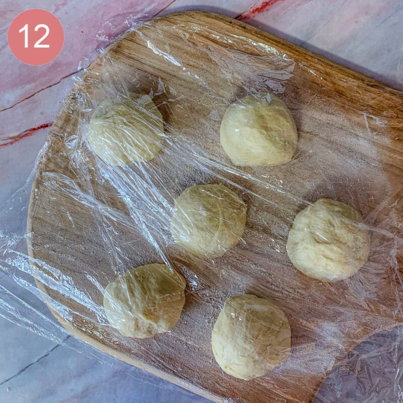 6 dough balls on a pizza peel covered in plastic wrap