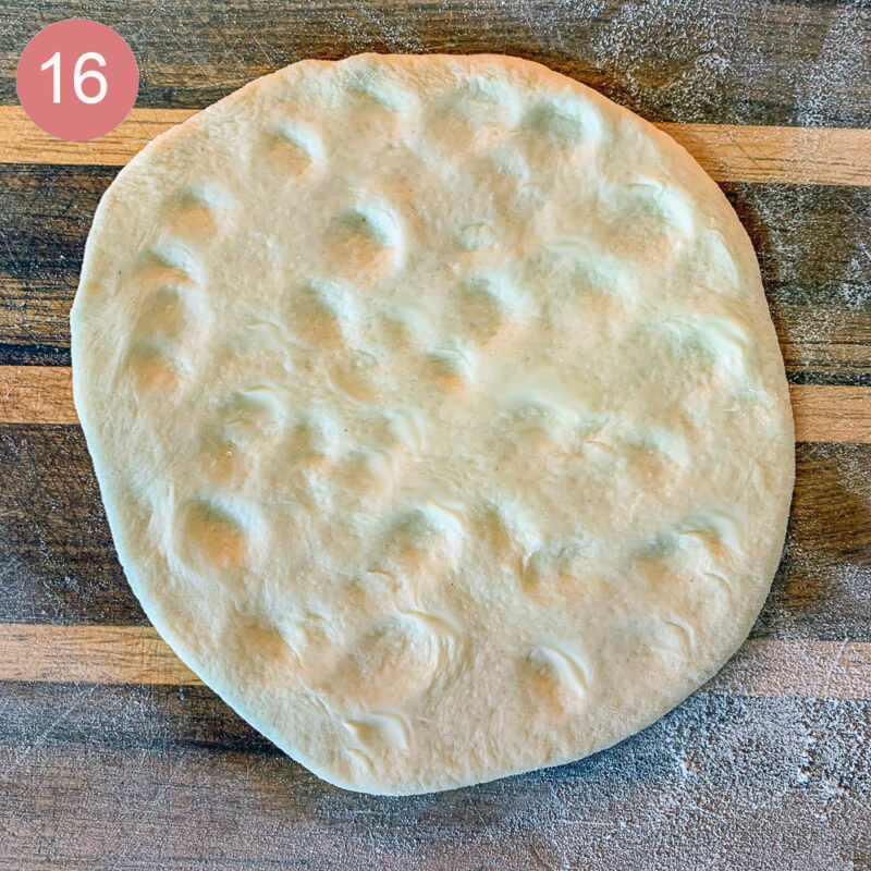 flat bread dough with indentations on a floured cutting board