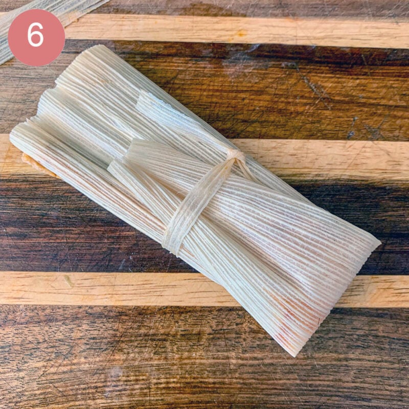wrapped tamale on a striped cutting board