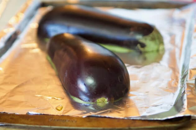 one eggplant sliced in half, flesh down on a baking tray