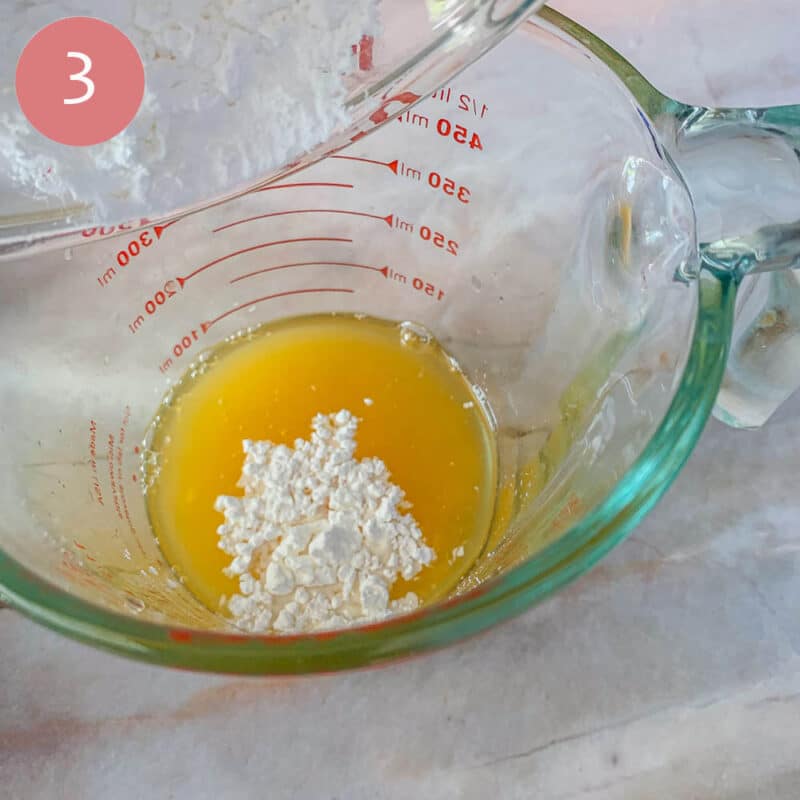 pouring cornstarch into a measuring cup with orange juice
