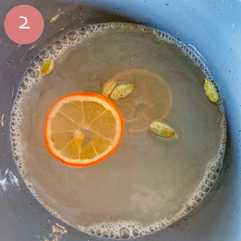 simple syrup in a pan with orange slices and cardamom pods