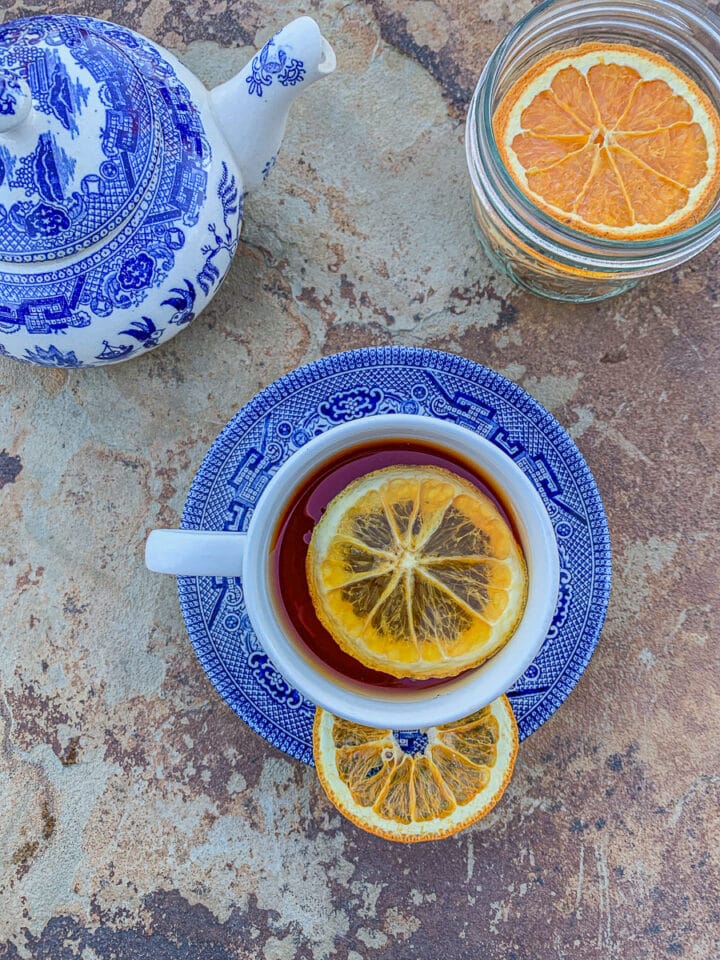 tea with orange slice in it alone with a blue teapot and more orange slices on the side