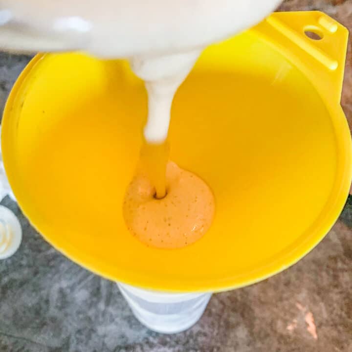 chipotle sauce being poured in a squeeze bottle through ha yellow funnel