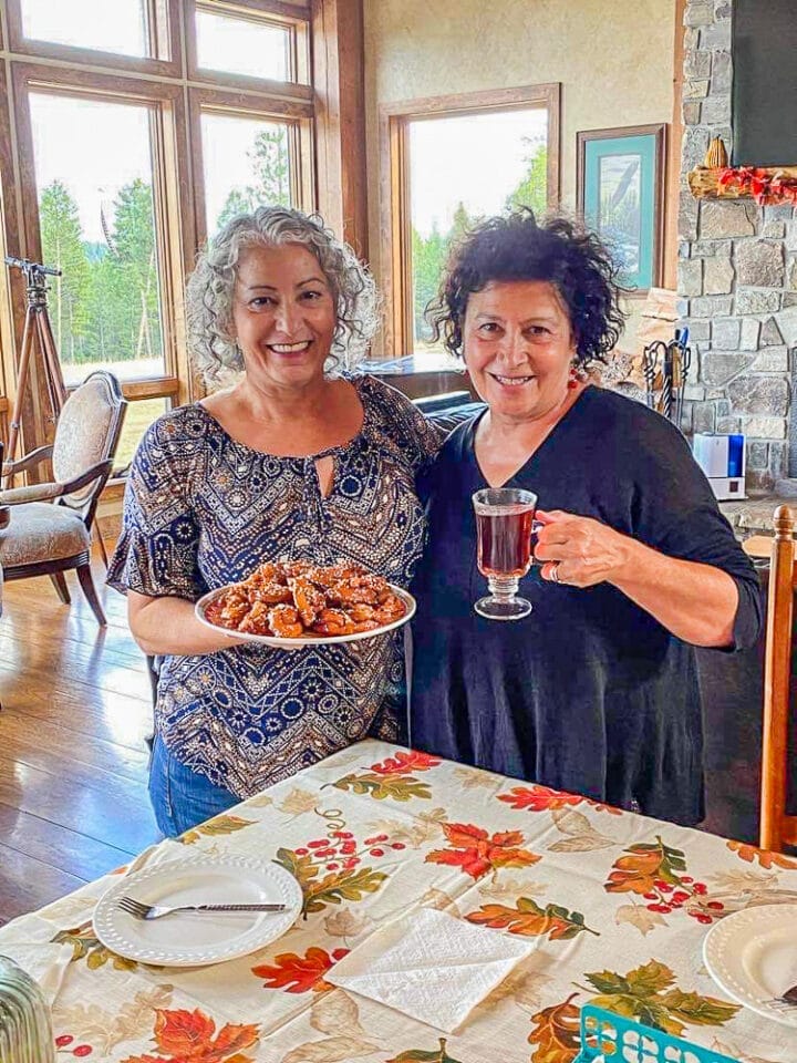 two ladies, one holding a plate of cookies, the other a glass of tea