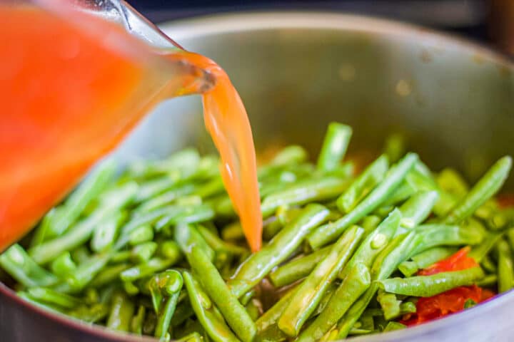 pouring tomato sauce over green beans in a pot