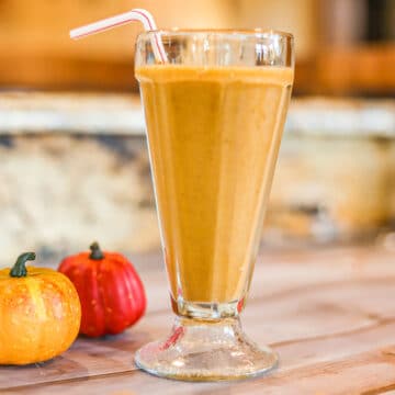 pumpkin protein shake in a tall glass with 2 small pumpkins next to it