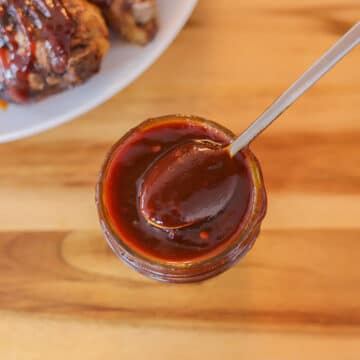 BBQ sauce in a small jar with bbq chicken in the background