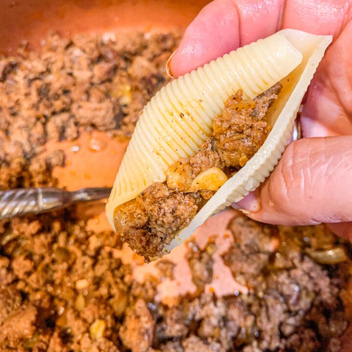 stuffed shell being held over seasoned ground meat