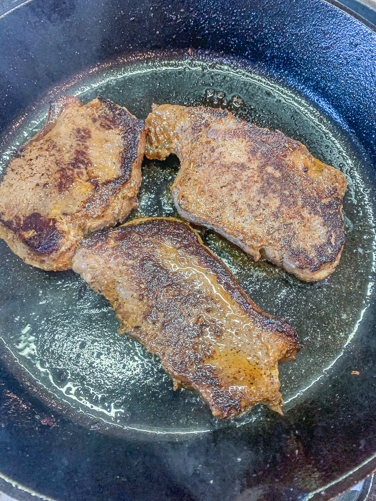 3 venison steaks cooking in a pan