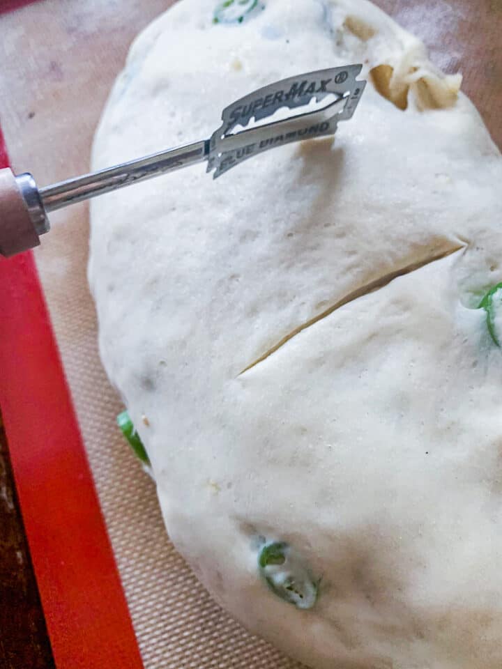 scoring a loaf of  jalapeno cheddar sourdough bread