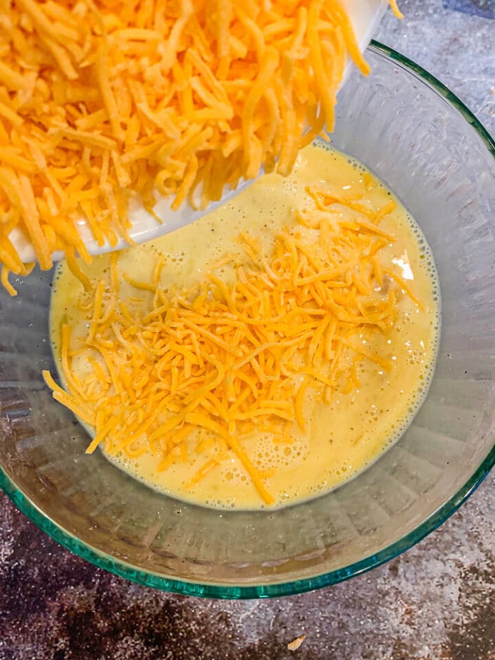 adding shredded cheese to whisked eggs in a bowl