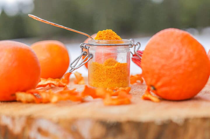 orange peel powder in a spoon on a wooden slab with oranges around it