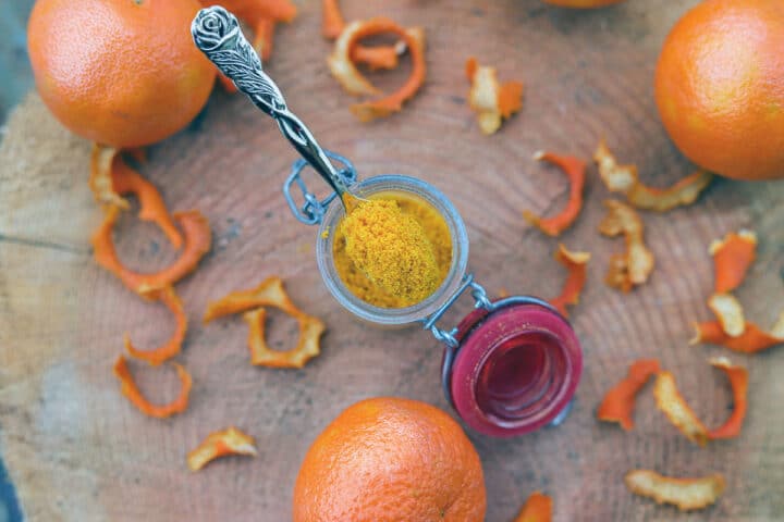 polvo de naranja en una cuchara sobre un frasco con otras naranjas alrededor