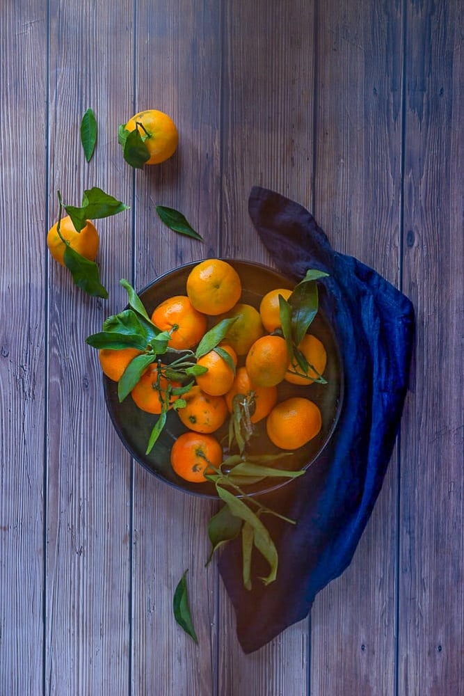 oranges in a plate with a blue cloth on one side of the plate