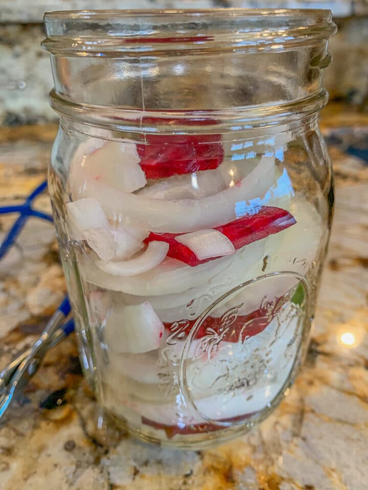 onions and beets being prepared in a jar for pickling
