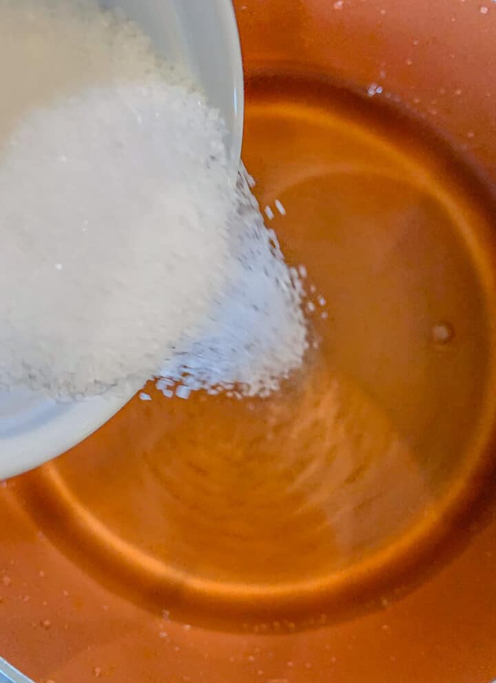 salt being poured into a pot of liquid